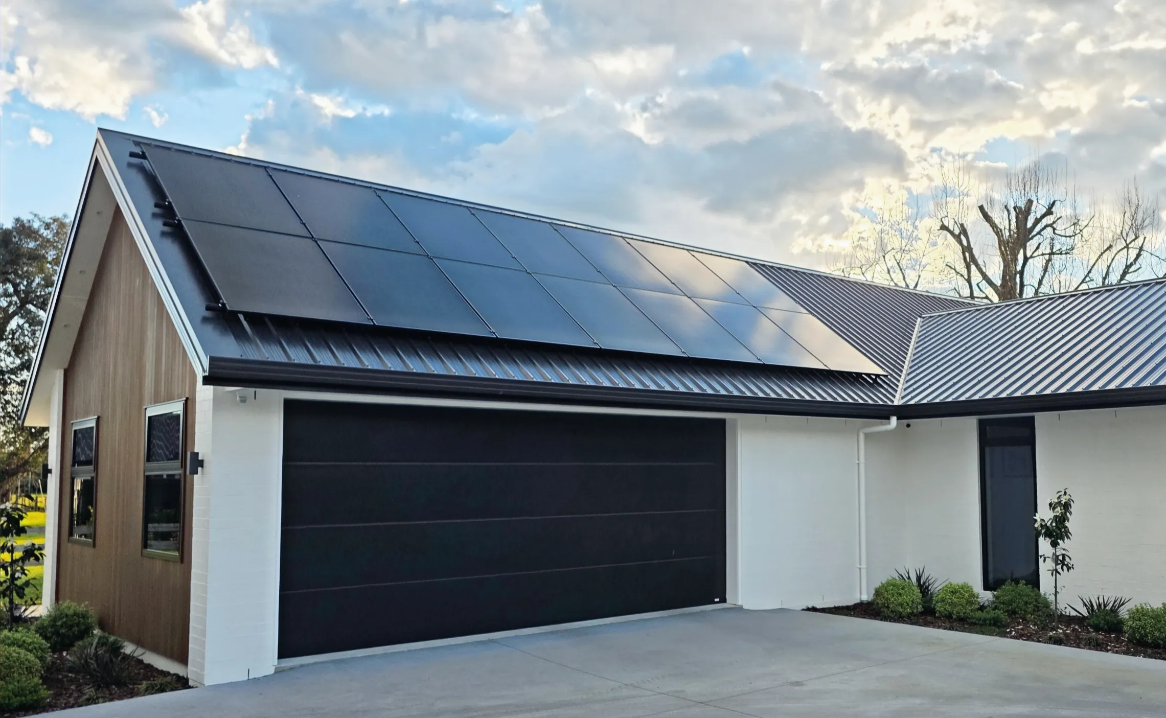 A black solar array installed across the roof of a cedar and plaster house on a clear day