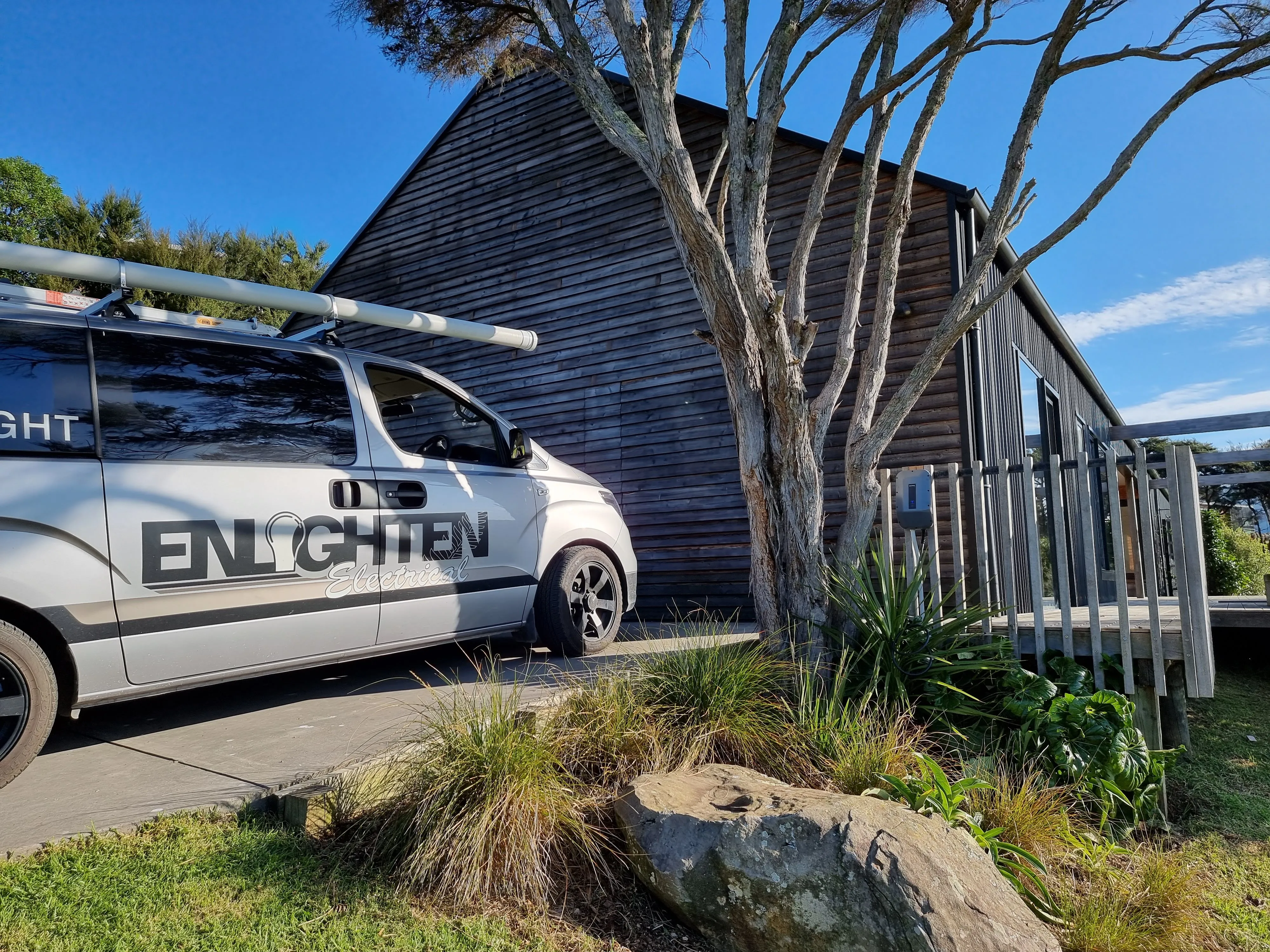 An Enlighten Electrical van parked outside a dark timber clad house on a clear day